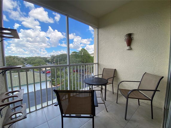 Balcony view with chairs and a table overlooking a residential area with trees and rooftops.
