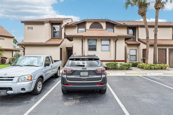 Front view of a residential building with multiple units, featuring a brown roof and beige exterior, with two parked cars in front.