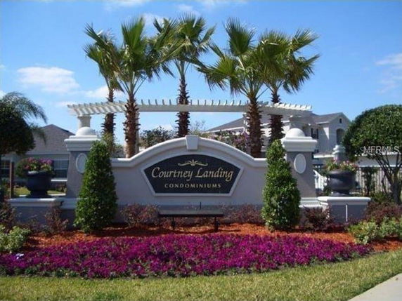 Front view of condominium entrance with sign and landscaping.