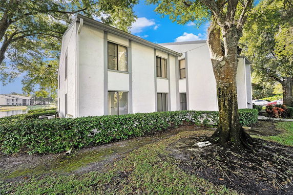 Side view of a two-story white building with trees and shrubs.