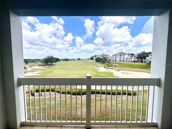 Framed view from a balcony overlooking a golf course and several buildings.