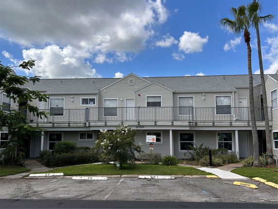 Front view of a two-story residential building with a balcony on the upper level and parking space in front.