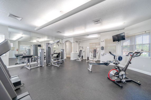 Indoor gym area with various exercise equipment and mirrors on the walls.