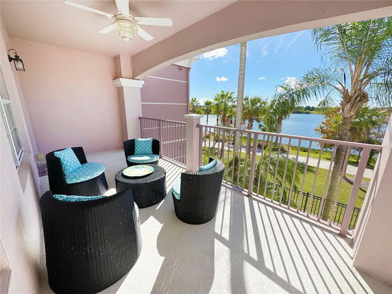 Outdoor balcony area with seating overlooking a scenic view of palm trees and a body of water.