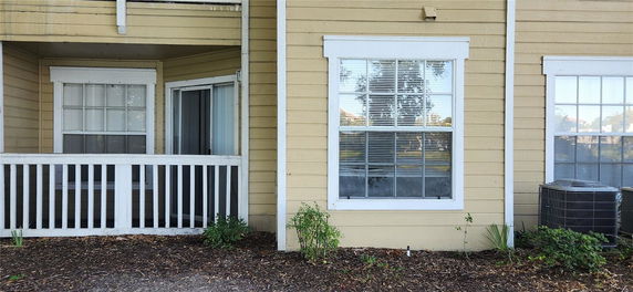 Front view of a house with beige siding, a window with white trim, and a small patio area.