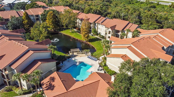 Aerial view of a residential complex with red-tiled roofs, a swimming pool, and a pond with a fountain.
