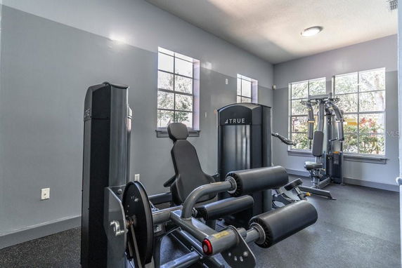Room with gym equipment including exercise machines, weight stations, and windows.