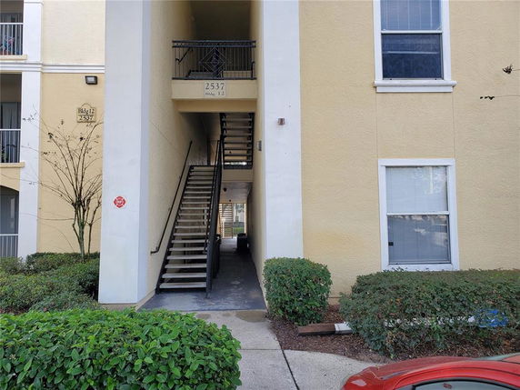 Front view of a multi-story building with an exterior staircase and yellow facade.