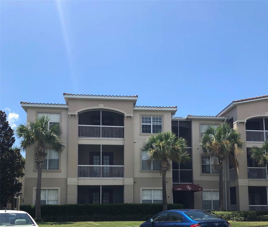 Front view of a three-story apartment building with balconies and palm trees.