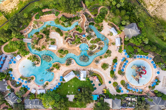 Aerial view of an outdoor swimming pool area with winding pools, palm trees, and lounge chairs.