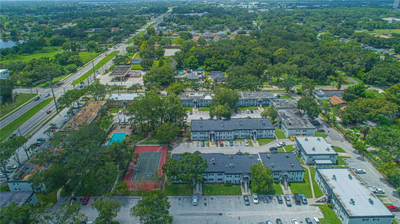 Panoramic view of a residential area with multiple buildings, parking spaces, swimming pool, and tennis court surrounded by trees.