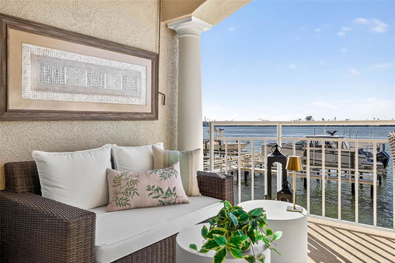 Outdoor terrace with wicker seating overlooking a waterfront view with boats and a railing.