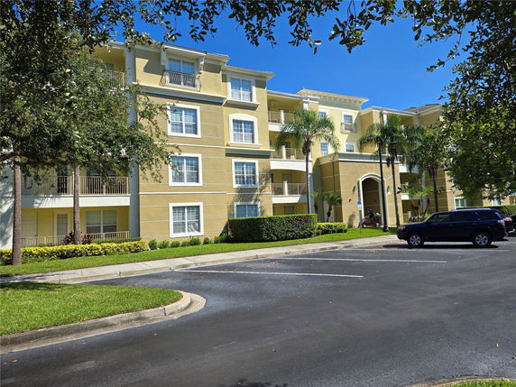 Front view of a multi-story apartment building with balconies and a parking area.