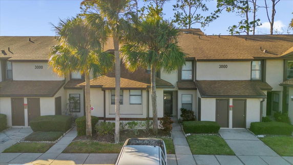 Front view of a two-story townhouse with brown roof and palm trees.