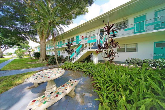 Front view of a two-story building with turquoise accents and staircases, surrounded by greenery.