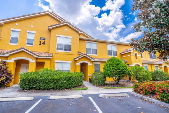 Front view of a yellow multi-story townhouse complex with visible parking area.