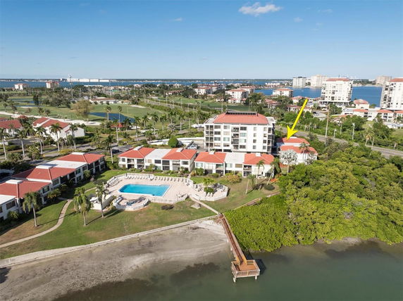 Aerial view of a residential complex near the waterfront with a central swimming pool and surrounding greenery.