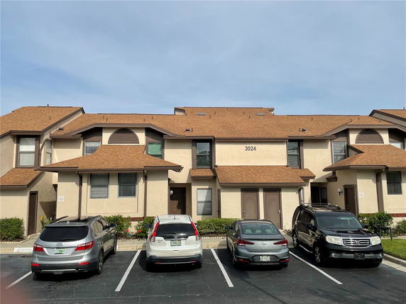 Front view of a two-story residential building with a brown roof and multiple parked cars in front.
