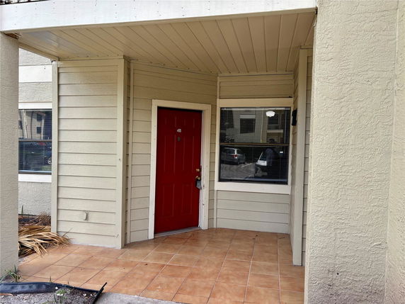 Front view of a house entrance with a red door and windows on a tiled porch.