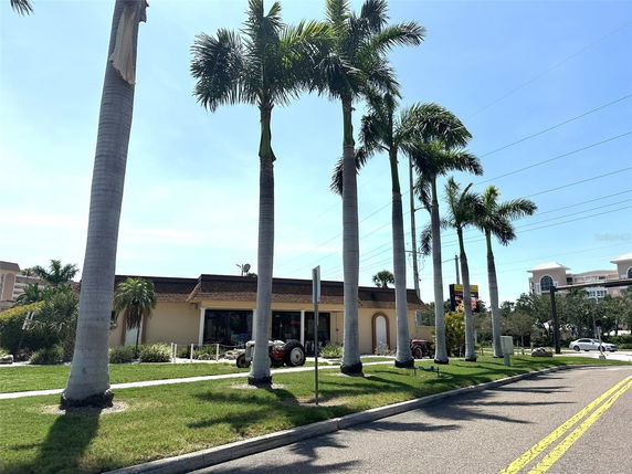 Front view of a single-story building with a flat roof and large windows, surrounded by palm trees.
