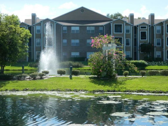 Front view of a multi-story apartment building with a fountain and landscaped area in front.
