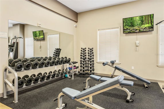 Indoor gym area with dumbbells, benches, and a wall-mounted TV.