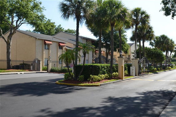 Front view of a multi-story building with palm trees and gated entrance.