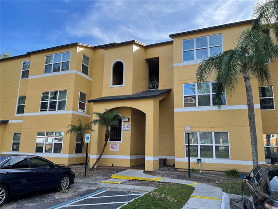 Front view of a yellow, multi-story apartment building with large windows.