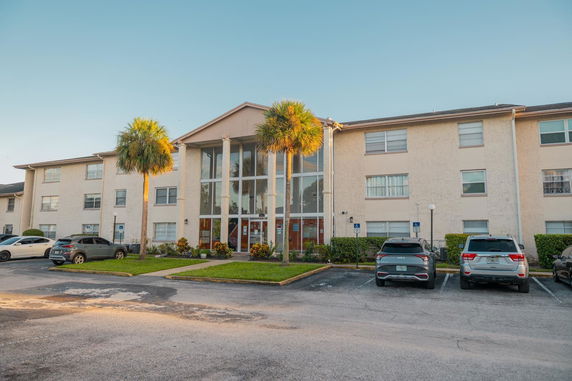 Front view of a three-story apartment building with large glass entrance and parking area.