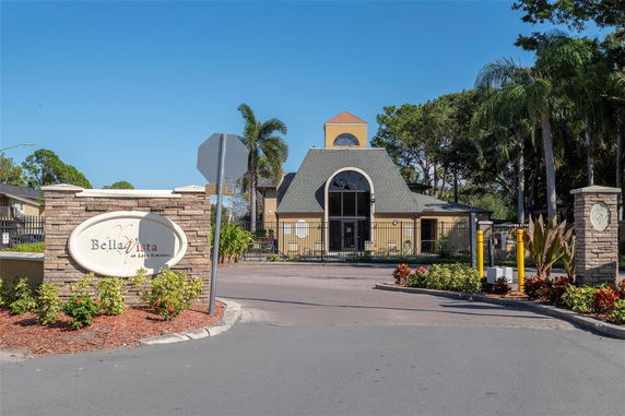 Front view of a building with a tower and arched entrance, surrounded by a fence and landscaped area.