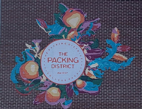 Exterior view of a building with a colorful mural on the brick wall featuring 'The Packing District' text.