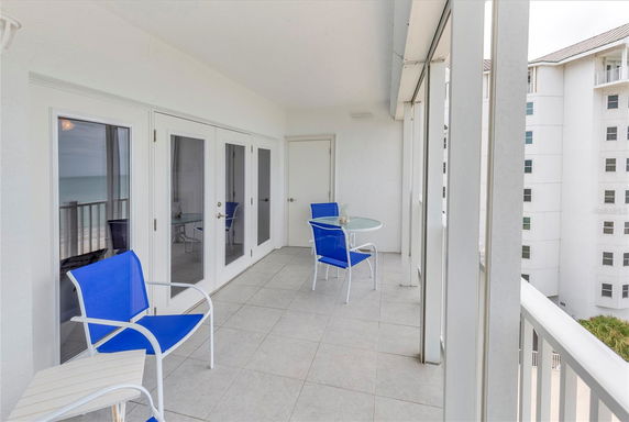 Balcony area with blue chairs and a small table, overlooking the ocean and adjacent building.