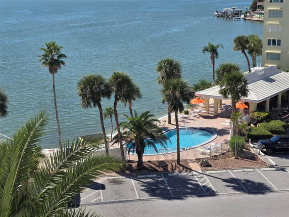 Panoramic view of a waterfront with a swimming pool and palm trees.
