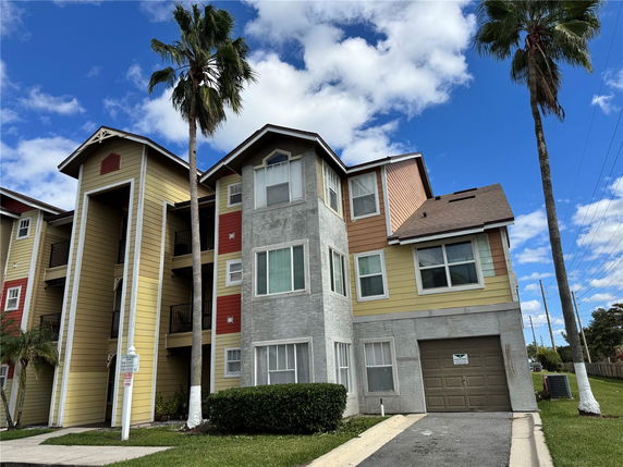 Front view of a multi-story residential building with a mix of yellow and gray exterior and a garage.