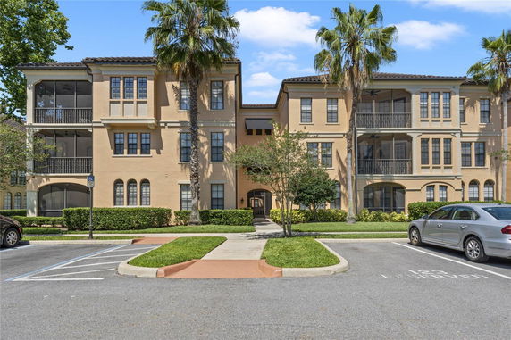 Front view of a three-story residential building with balconies and palm trees.