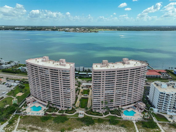 Panoramic view of twin apartment buildings by the water, featuring swimming pools and rooftop units.