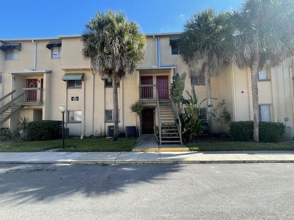 Front view of a multi-story apartment building with exterior stairs and palm trees.