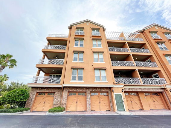 Front view of a multi-story apartment building with balconies and garage doors on the ground level.
