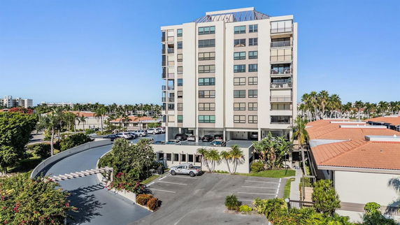 Front view of a multi-story apartment building with balconies and surrounding parking area.