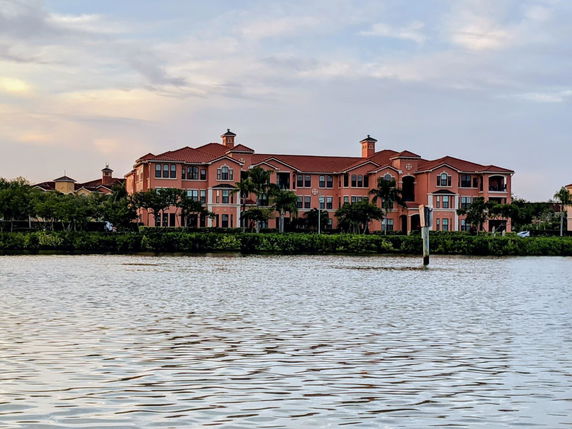 Front view of a multi-story building with a red tile roof facing a body of water.