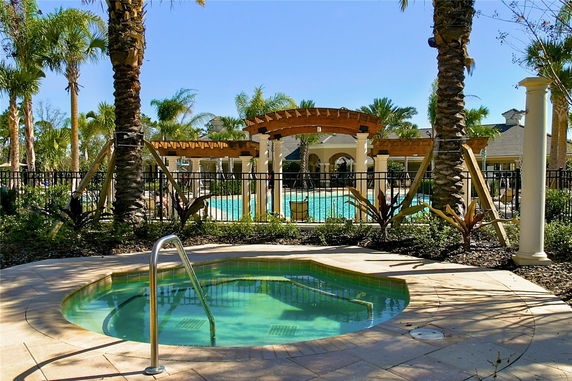 Outdoor swimming pool area with a hot tub and palm trees.