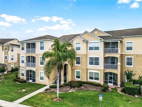 Front view of a multi-story apartment building with balconies and a landscaped lawn.