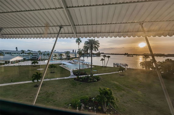 Panoramic view of a waterfront area with a dock, pool, and distant buildings under a setting sun.