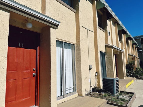 Front view of a row of two-story houses with red doors and cream-colored walls.