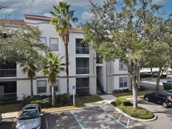 Front view of a three-story residential building with balconies and surrounded by trees.