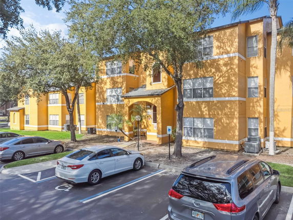 Front view of a three-story residential building with yellow exterior and multiple parked cars.