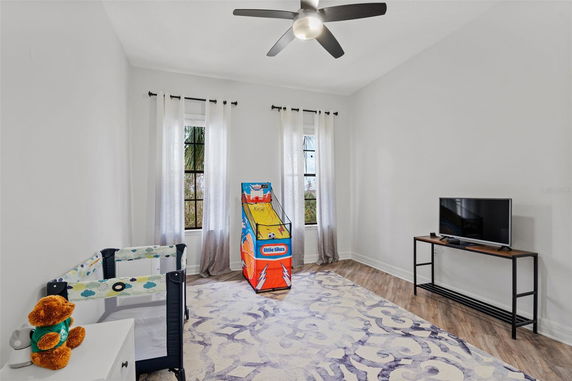 Room with a play area featuring a small basketball game, a playpen, and a TV on a stand.
