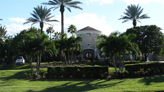 Front view of a two-story house with a round tower and palm trees.