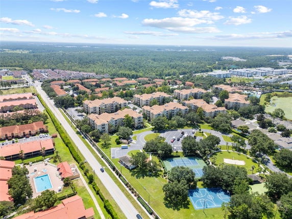 Panoramic aerial view of a residential complex with multiple buildings, a swimming pool, and sports courts.