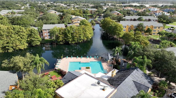 Panoramic view showing a pool area and buildings surrounded by trees and water bodies.